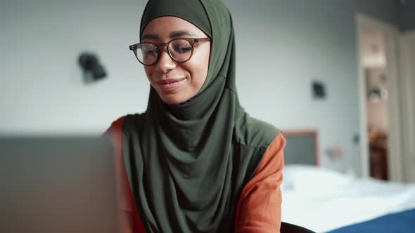 Muslim happy woman wearing eyeglasses typing by laptop