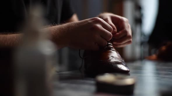 Closeup of Male Shoemaker Tying Laces on Repaired and Polished Light Brown Leather Shoes