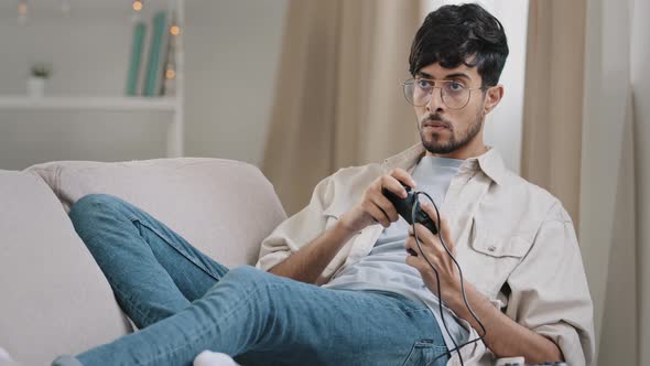 Arab Millennial Guy Bearded Indian Man Wears Glasses Lying Sofa Playing Console Enjoy Online Video