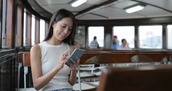 Woman using app of smart phone and taking boat in Hong Kong city 