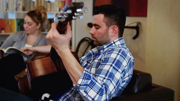 Man playing guitar while woman reading book