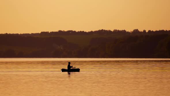 Silhouette of a man with fishing rods in the middle of the lake at sunset.