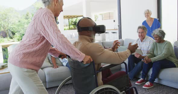 Happy senior diverse people with man in wheelchair using vr headset at retirement home