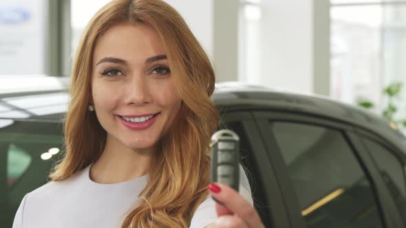 Cheerful Attractive Woman Smiling Showing Car Keys To the Camera at the Dealership
