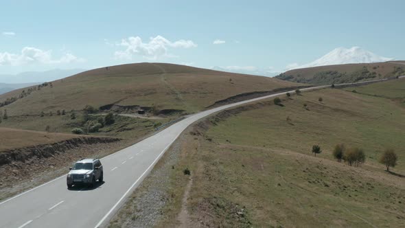 Grey Suv Tourist Car Drives Along Empty Asphalt Road Stretching Travel Among Fields on Green Hills