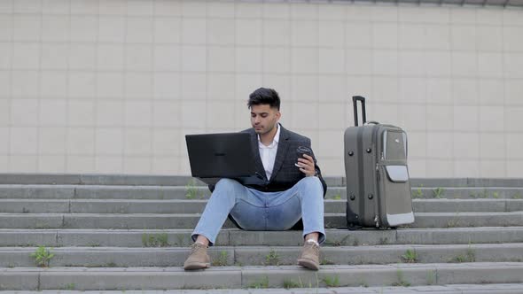 Young Arab Businessman Working on His Laptop Computer While Sitting on the Stairs in the Street with