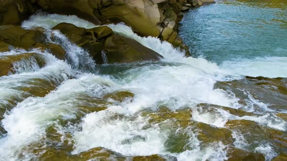 Mountain river with clear turquoise water falling down in cascades between wet boulders with