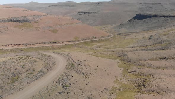 aerial shot following two mountain bikers climbing up a gravel road mountain pass