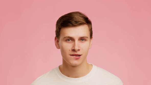 Playful Millennial Guy Biting Lips Posing Over Pink Background