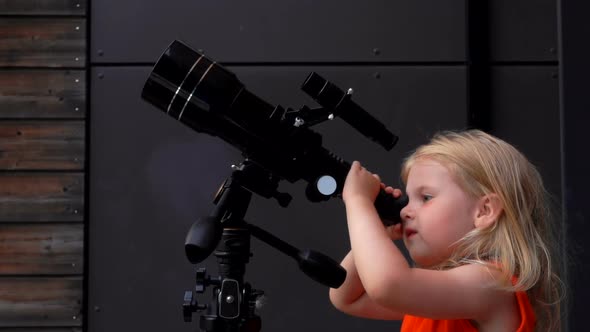 A Little Girl in the Orange Top is Exploring the Sky Through a Telescope