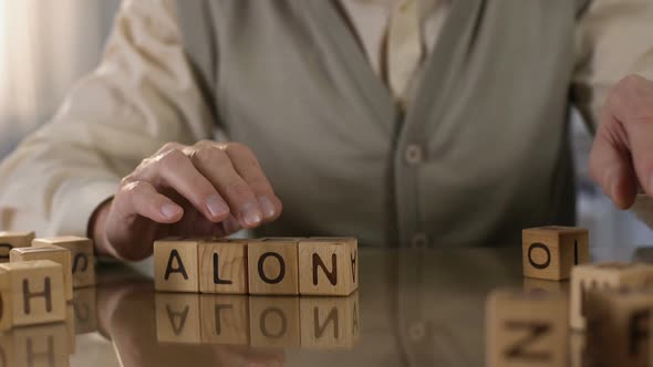 Old Wrinkled Male Making Word Alone of Wooden Cubes on Table, Nursing Home