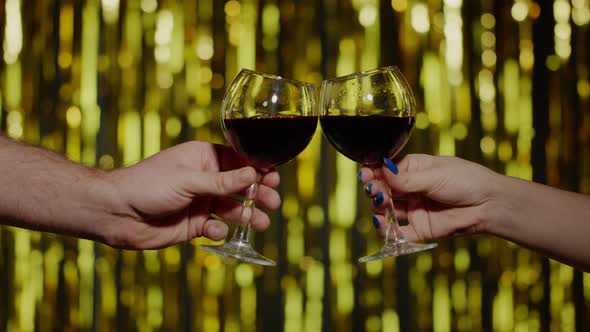 Two Hands with Glasses of Red Wine Making Cheers Raising Toast on Gold Background in Slow Motion