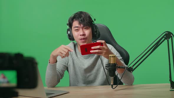 Camera Recording Video Of Asian Man With Headphone Playing Mobile Phone Game On Green Screen