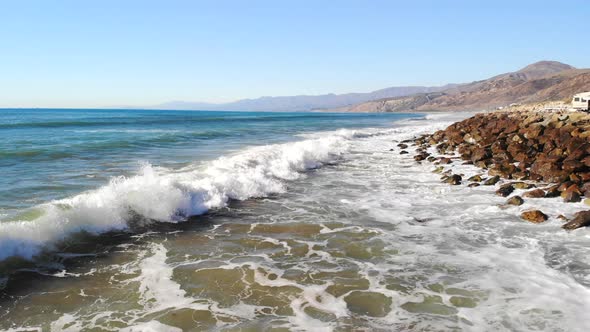 Epic aerial drone shot from a blue crashing ocean wave to a view overlooking the golden California c