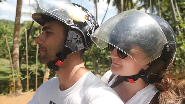 Happy Young Couple in Helmets Rides an Motor Scooter Along Country Road. Smiling Man and Woman