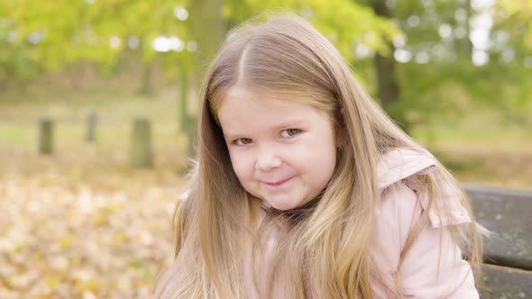 Cute Little Caucasian Girl Smiles Shyly at the Camera As She Sits on a Bench in a Park  Closeup