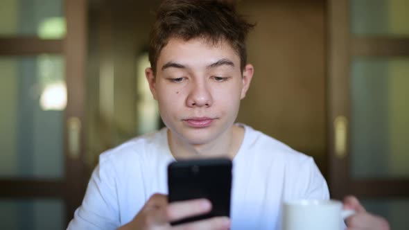 sleepy teenager chatting on a smartphone while having breakfast and drinking tea