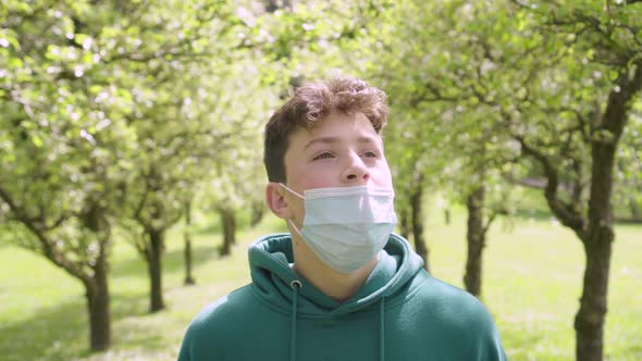 A young man in a fruity spring blooming garden takes off his protective medical mask