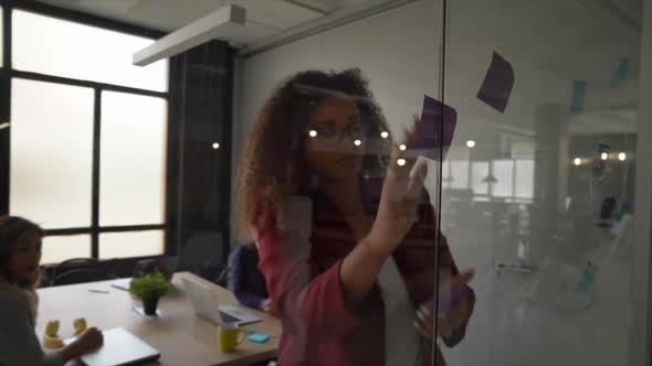 Woman putting sticky notes on glass pane in team meeting