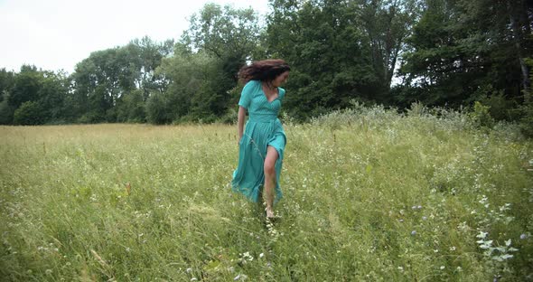 A Girl In A Long Dress Runs Across A Green Meadow