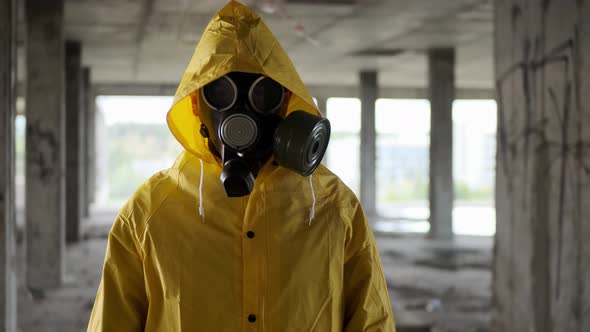 Man in Black Gas Mask Looks at Camera and Holds Out His Hand in Abandoned Building