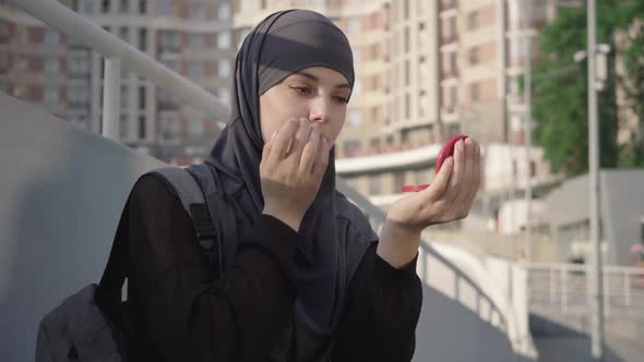 Portrait of Beautiful Brown-eyed Muslim Woman Correcting Makeup Outdoors. Charming Young Middle