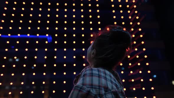 Young Woman is Very Emotionally Looking at Glowing Houses on the Street of the Evening City Admires