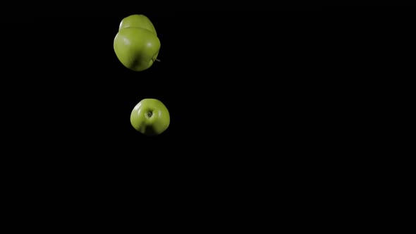 Close Up at the Group of Three Green Apples Fly Up and Spinning on a Black Background in Slow Motion