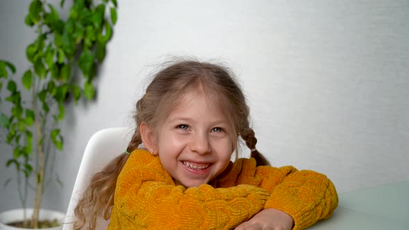 a Little Blonde Girl with Pigtails in a Yellow Sweater at the Table Smiling Happy Child