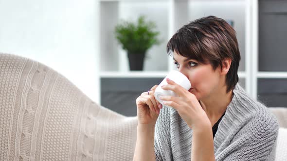 Pensive Beautiful Mature Female in Warm Sweater Drinking Tea Relaxing at Home Medium Closeup