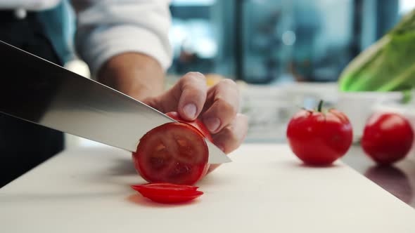 Professional restaurant kitchen, close-up: Chef cuts tomatoes with a knife