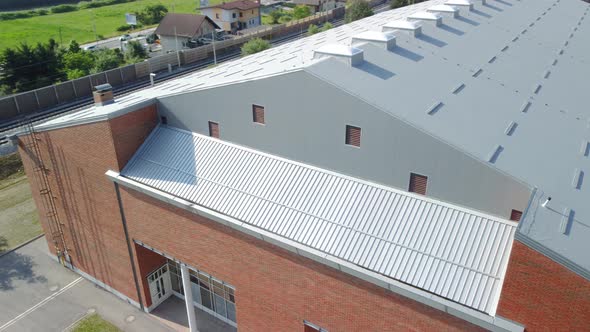 Flying beside red clay bricks build sports hall with grey insulation panels used for roof top. Aeria