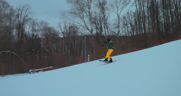 Snowboarder Quickly Rides From a Snowy Slope and Raises the Board Up