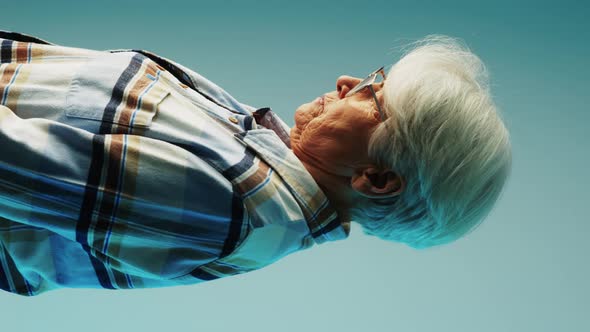 Vertical Shot of an Elderly Woman Sad Looking to the Light Source Over Blue Studio Background