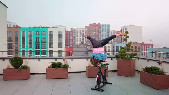 Athletic Woman Makes Twine Training Routine on Spinning Stationary Bike on House Roof Weight Loss