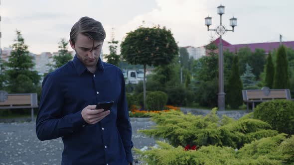 Bearded Man Looks on His Black Phone and Smiles