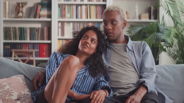 Happy Beautiful Interracial Couple Hugging Relaxing on Sofa in Cozy Apartment