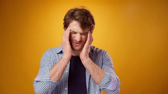 Young Man Suffering From Headache Touching Head Yellow Background