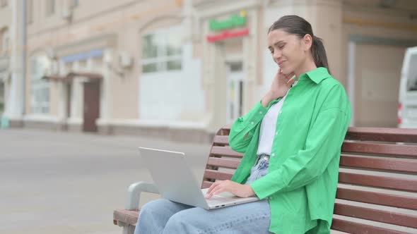 Hispanic Woman with Neck Pain Using Laptop While Sitting Outdoor on Bench