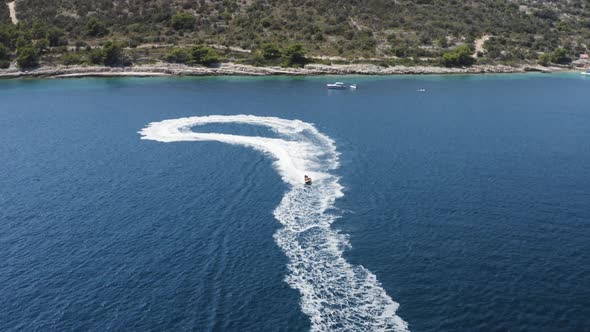 An aerial drone shot of someone on a jet ski, going fast. Featuring the coastline, the ocean and wav