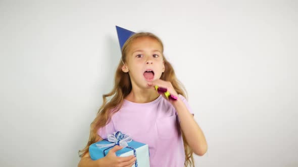 Birthday Kid Holds a Gift and Blows Noisemaker.Young Girl Wearing Birthday Cap Over White Background