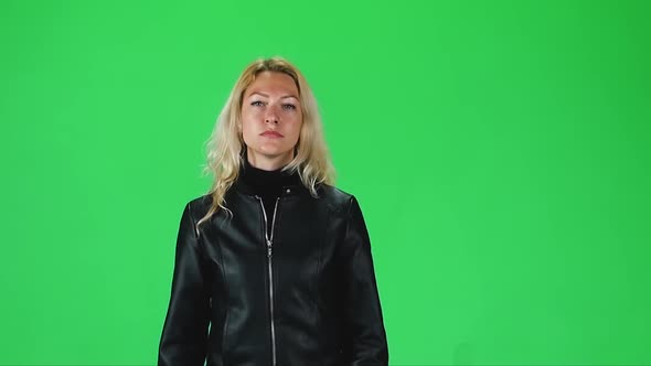 Blonde Girl in Black Leather Jacket Going and Looking Straight Into the Camera Against a Green