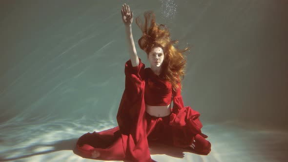 Attractive Redhaired Young Woman Swims Beautifully Underwater in a Red Dress