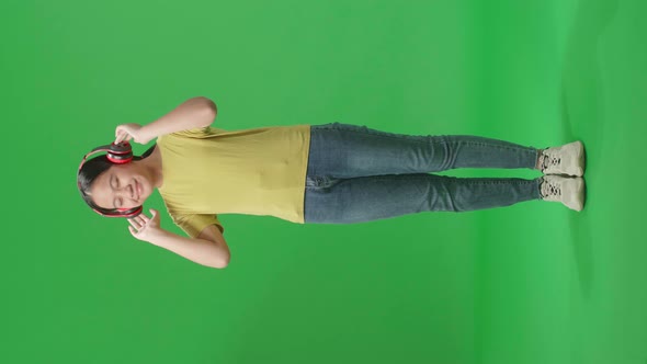 Full Body Of Young Asian Kid Girl Listening To Music With Headphones And Dancing In The Green Screen