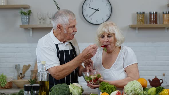 Senior Woman and Man Feeding Each Other with Fresh Raw Vegetable Salad. Eco Food Eating Diet