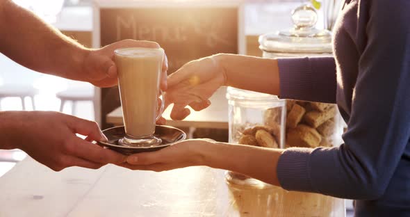 Mid section of waiter serving a cup of cold coffee to customer