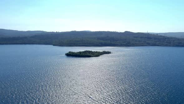 Small island with green trees in the middle of the lake with the pine forests in the background and