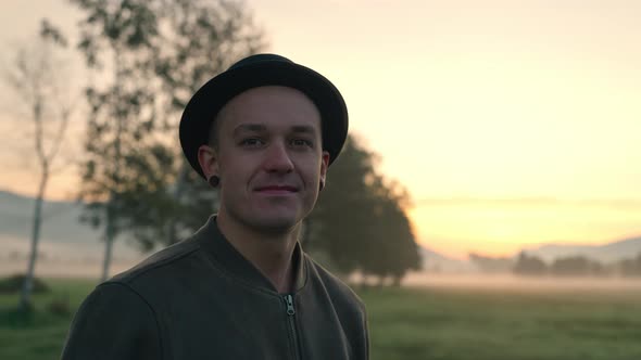 Young Man In Hat Standing Meadow On Misty Morning