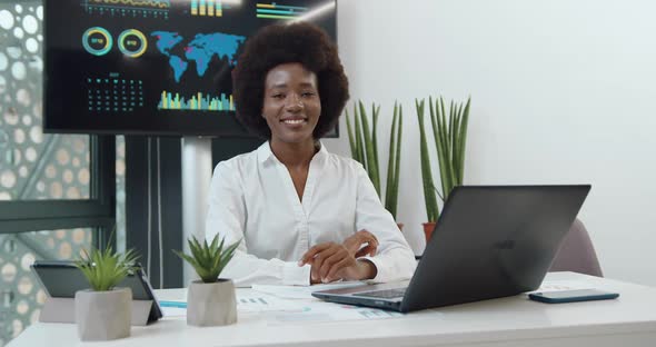 Young Black-Skinned Businesswoman with Afro Hairstyle Poses on Camera with Sincerely Smile