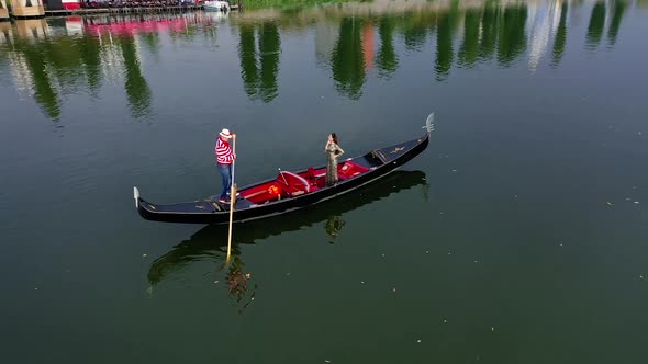 Gondolier riding a boat with a woman. Beautiful lady travelling in gondola along the river at sunset